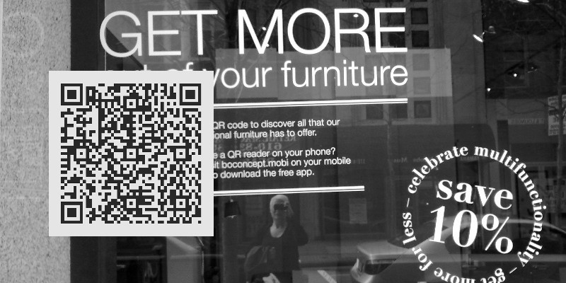An photo of a shopfront window with some text and reflection of the person. There is a large obviously-CGI QR code overlaid on part of the shopfront.